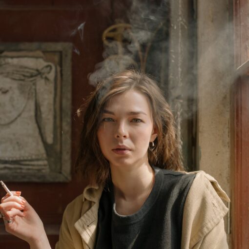 woman in black crew neck shirt and brown coat holding cigarette stick