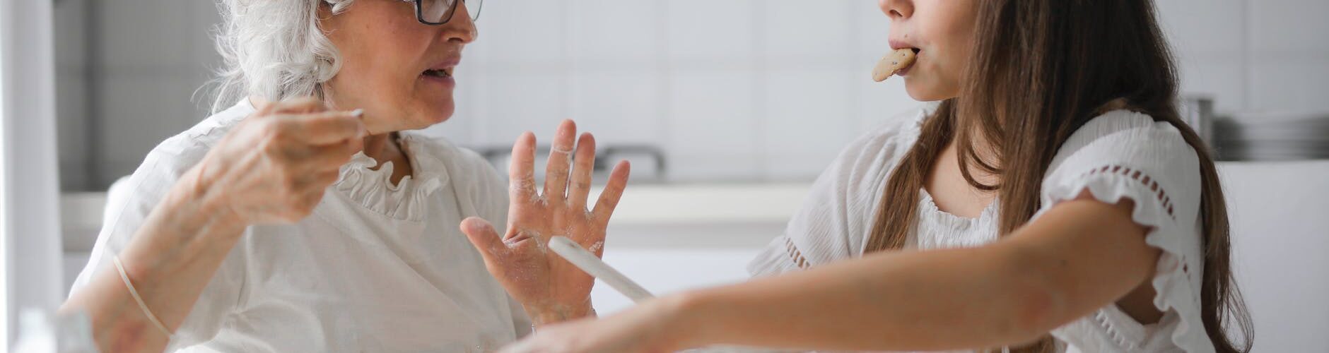 pensive grandmother with granddaughter having interesting conversation while cooking together in light modern kitchen