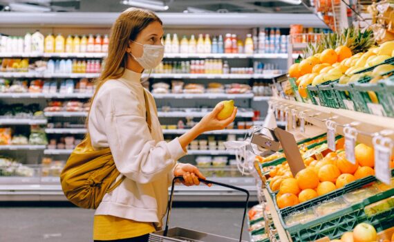 woman in yellow tshirt and beige jacket holding a fruit stand
