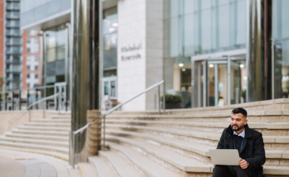 serious ethnic manager with laptop on city staircase