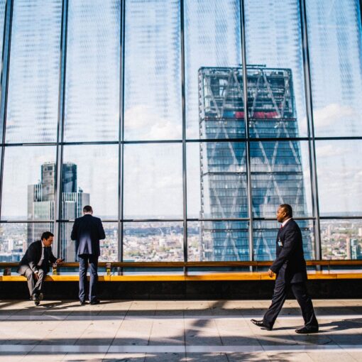 man walking on sidewalk near people standing and sitting beside curtain wall building