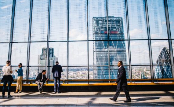 man walking on sidewalk near people standing and sitting beside curtain wall building