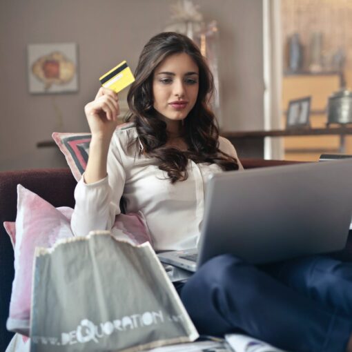 woman holding card while operating silver laptop