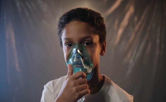 a boy in white shirt holding green oxygen mask