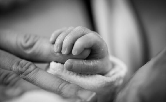 grayscale photography of baby holding finger