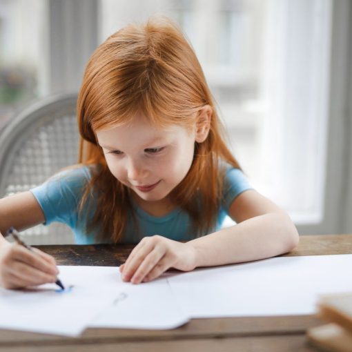 diligent small girl drawing on paper in light living room at home
