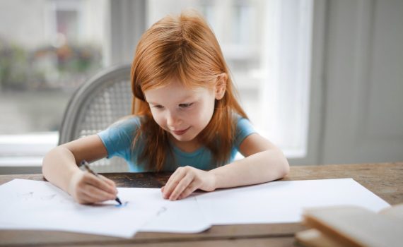 diligent small girl drawing on paper in light living room at home