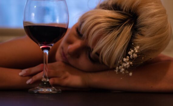 woman with white flower accent headdress leaning her head on table beside half filled wine glass