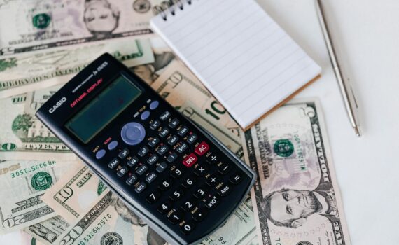calculator and notepad placed on usa dollars stack