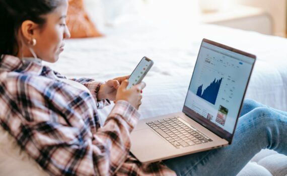 crop ethnic trader with smartphone and laptop on bench indoors